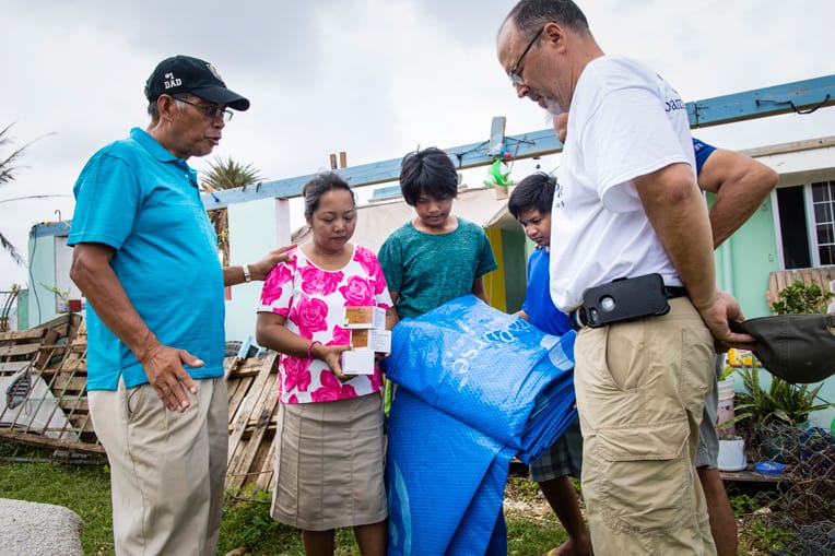 Pastor Manuelito Ray, left, of Cornerstone Community Church in Saipan prays for a family who received tarps and solar lights from Samaritan's Purse.