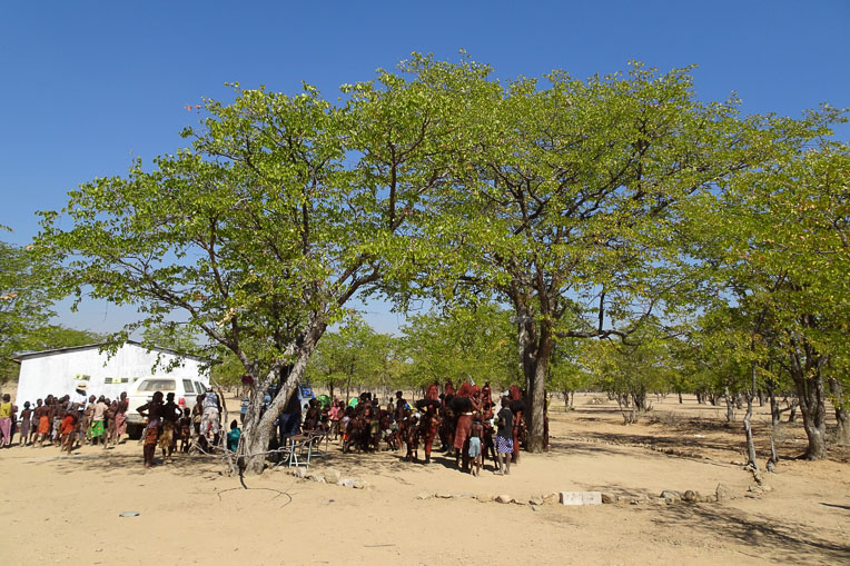 Himba villagers gather between their first church—the tree encircled by rocks—and their new church building (left).