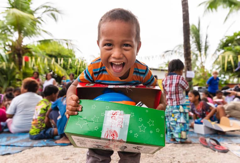 A child excitedly shows his shoebox after receiving the special gift during an outreach event in his village.