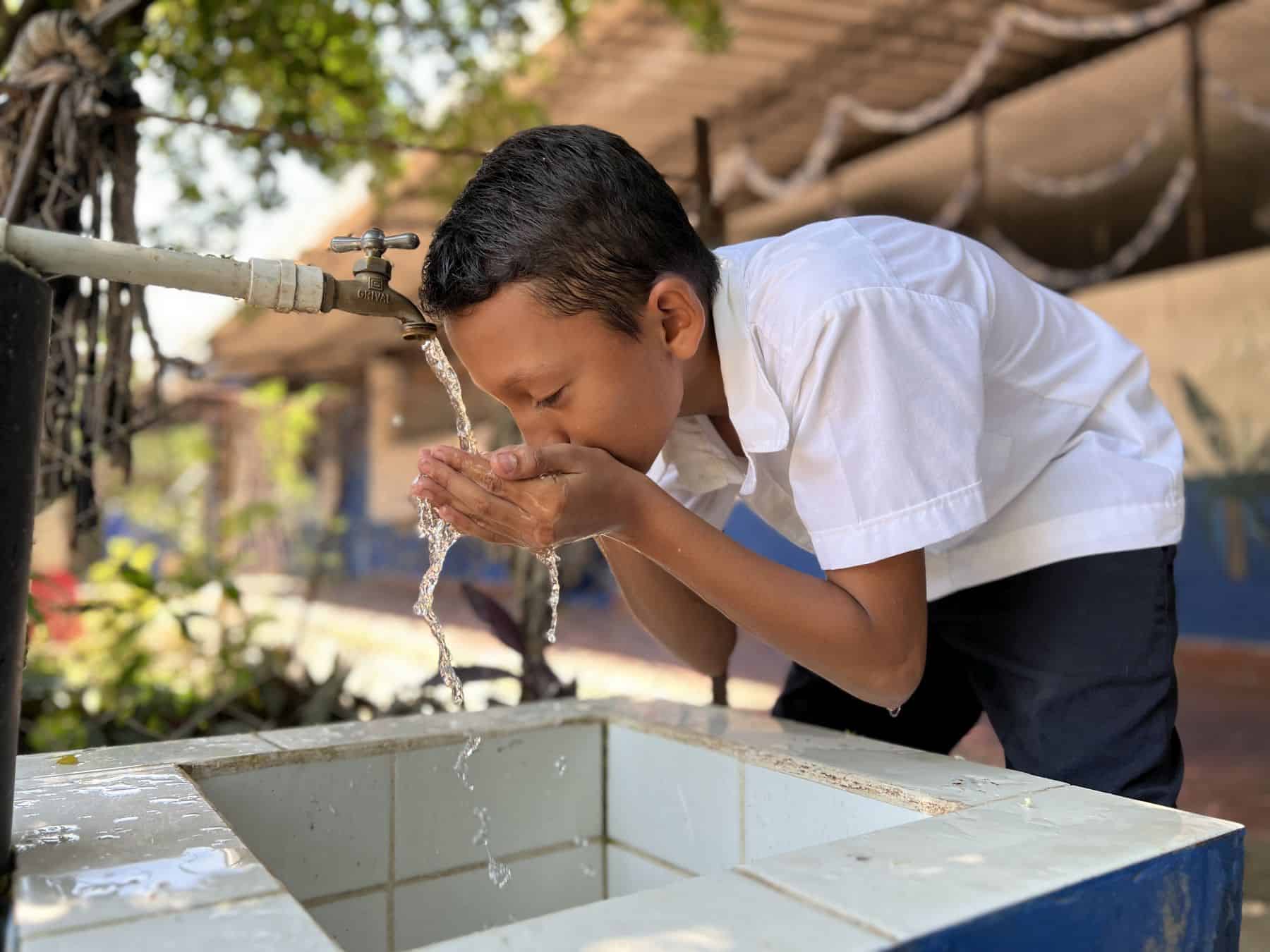 Hansel gets water from a tap connected to a large BioSand Water Filter now installed at his school in El Salvador. The filter meets the daily safe water needs of staff, students, and community members.