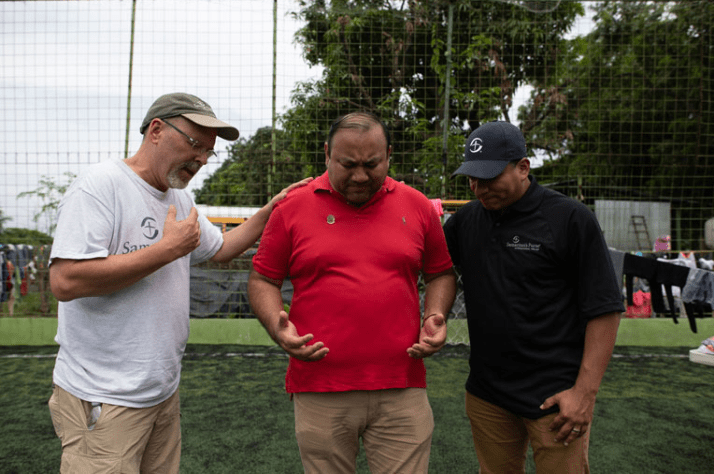 Samaritan's Purse staff John Freyler (left) and Angel Jordan (right) pray with Pastor Marlon Hamilton, one of our local partners.